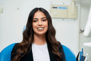 A smiling patient with metal braces sitting in an orthodontist's chair