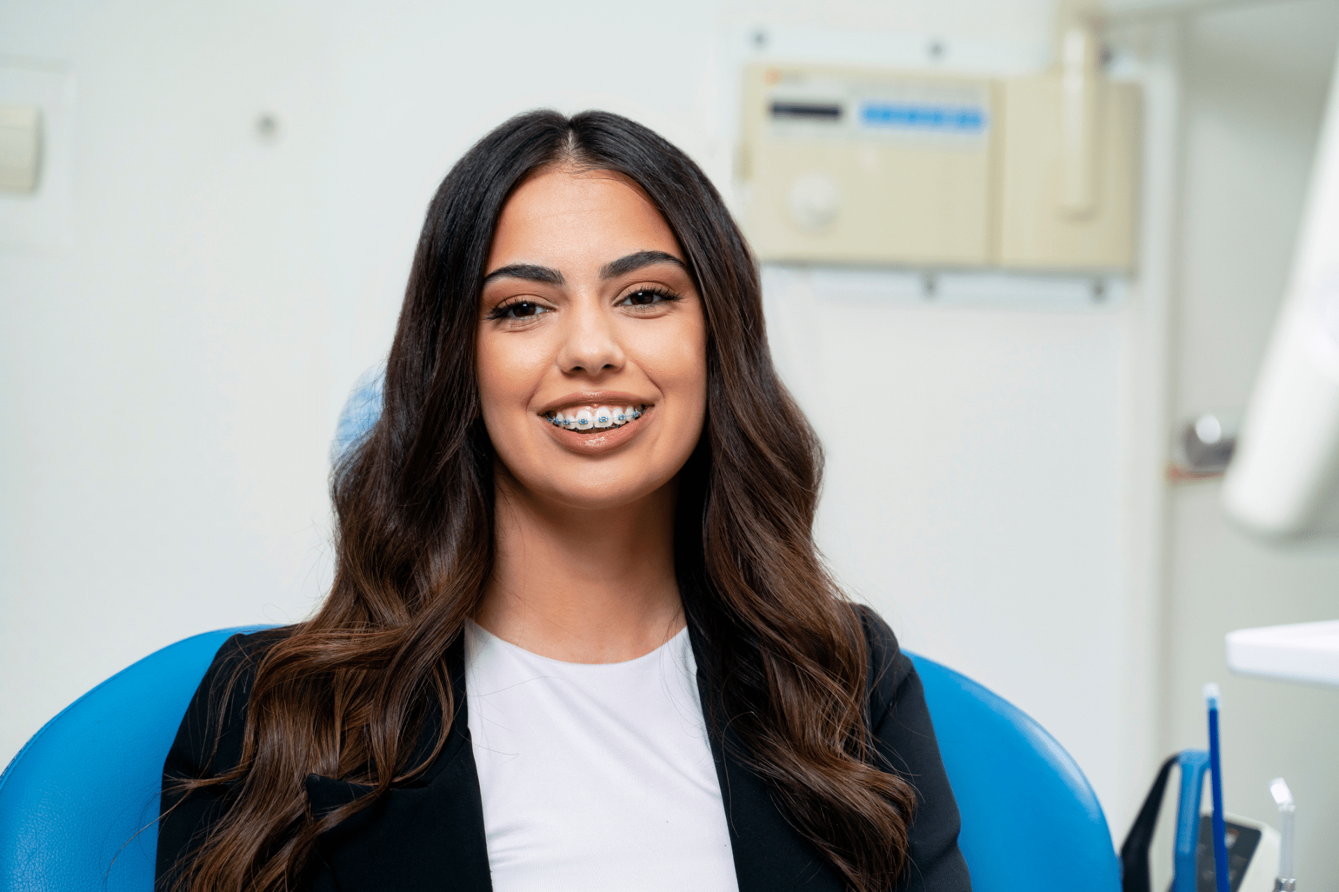 A smiling patient with metal braces sitting in an orthodontist's chair