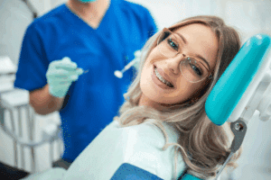 A smiling patient with braces and glasses in an orthodontist's chair, illustrating a guide on how often you need to visit the orthodontist.